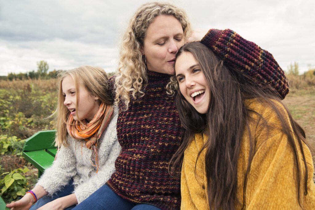 Mother kissing teenage daughter strolling in trailer in field.